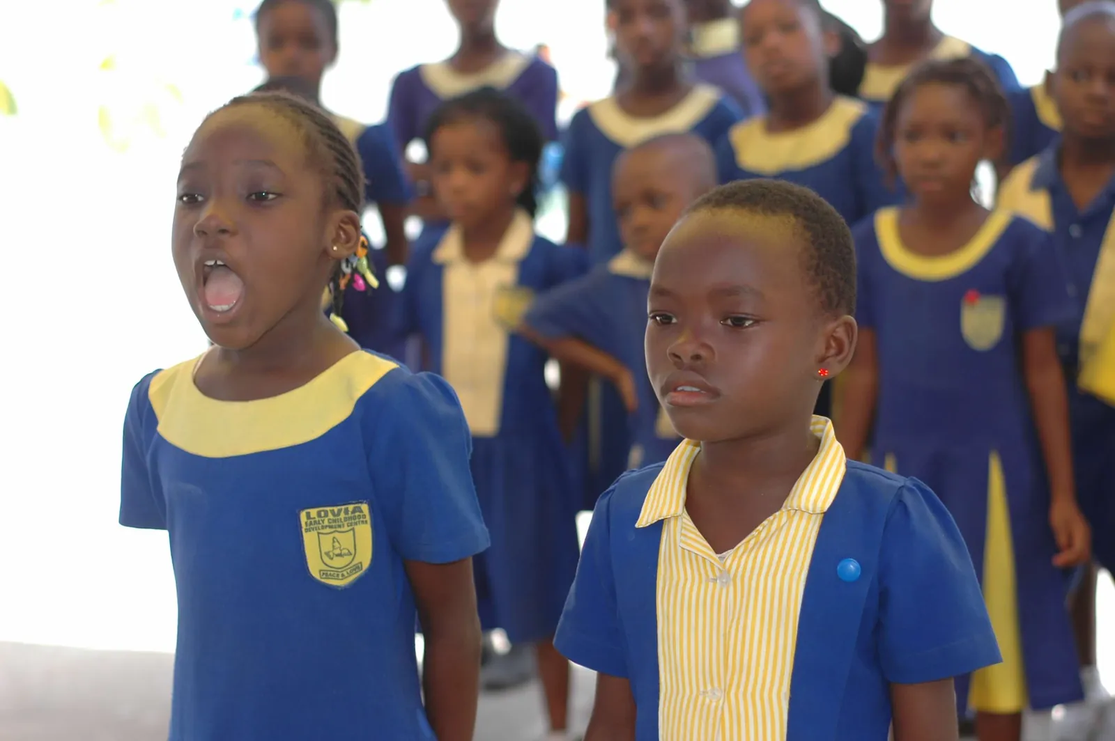 Two Lovia pupils in school uniform singing during a school gathering.